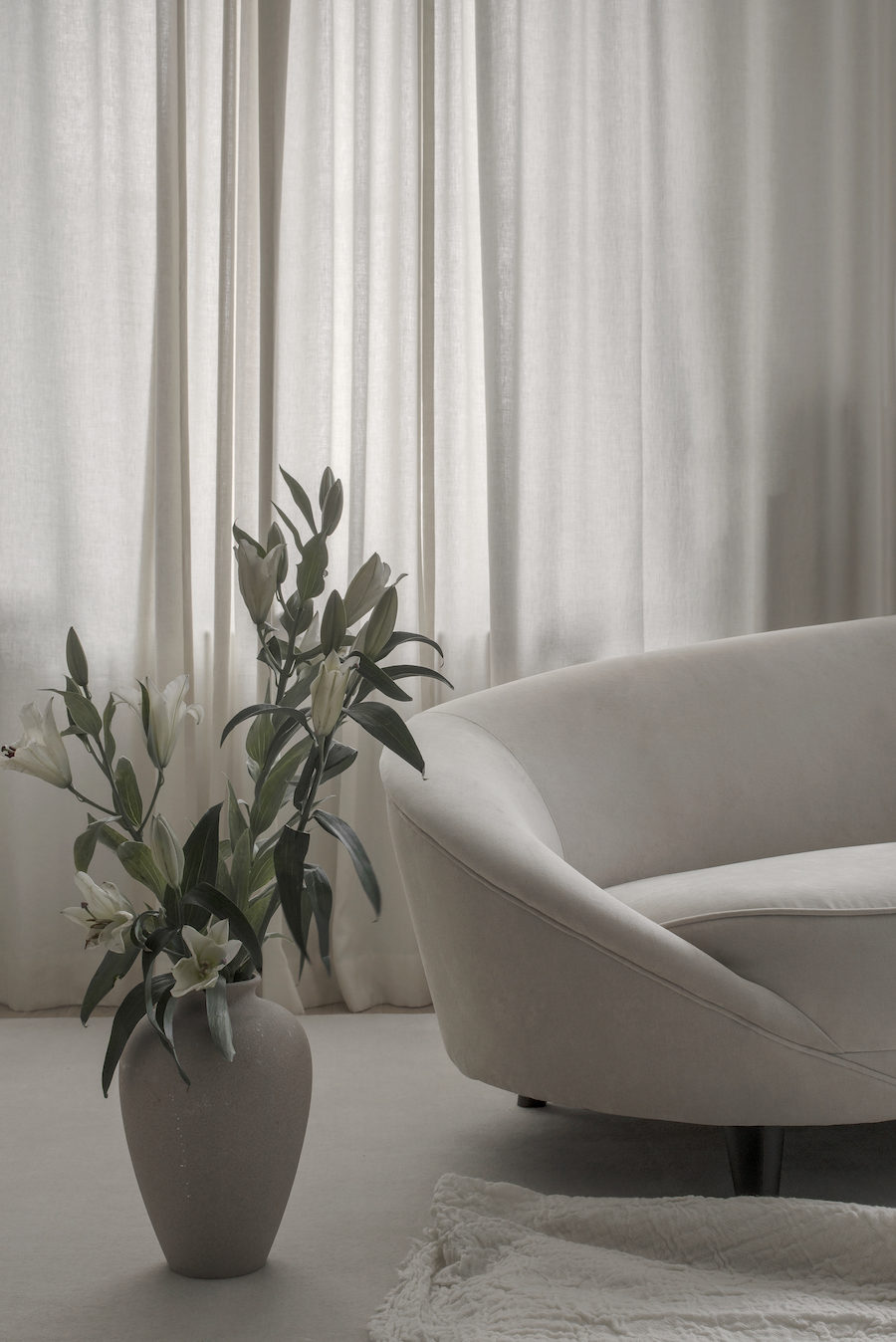 Närbild på soffa, och beige kruka med blomma.