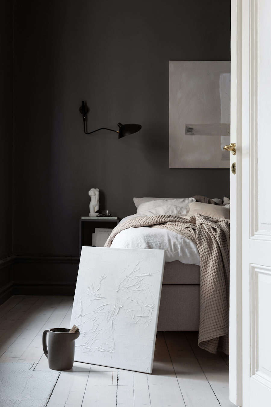 Tavla av Lovisa Häger för Wall of Art lutad mot säng i mörkt sovrum.
